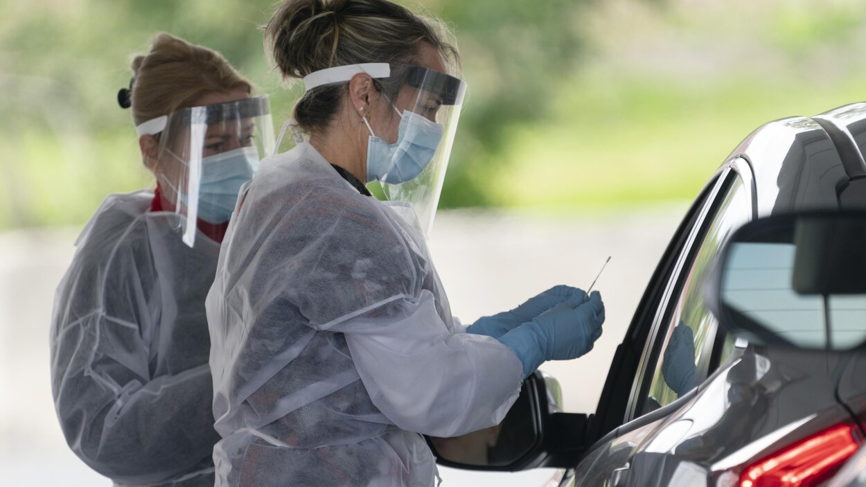 Deux infirmières masquées et gantées s'entretiennent avec un automobiliste.