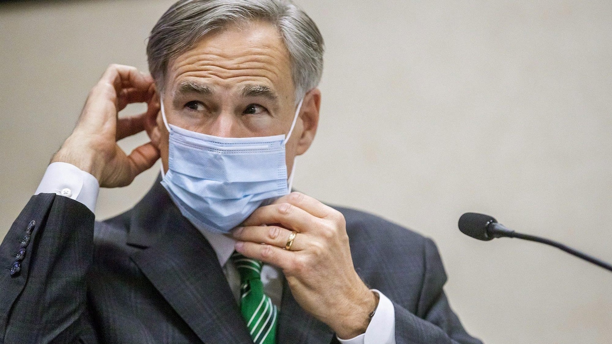 Greg Abbott replace son masque sur son visage.