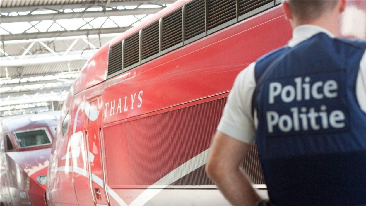 Un homme désigné comme un policier devant un wagon rouge sur lequel on peut lire Thalys.