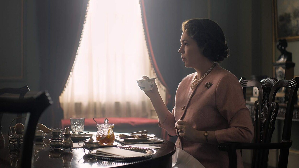 L'actrice, vêtue de rose, tient une tasse de thé dans une main.