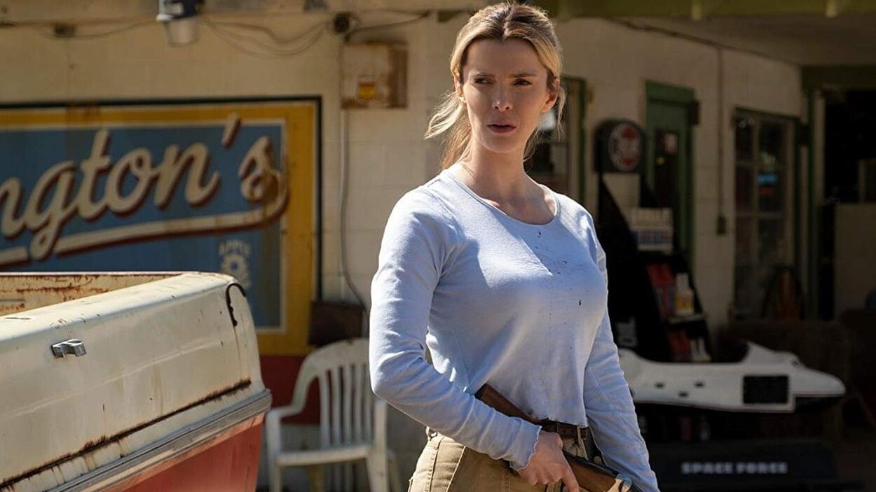 Une femme aux cheveux blonds tient un fusil dans une station service.