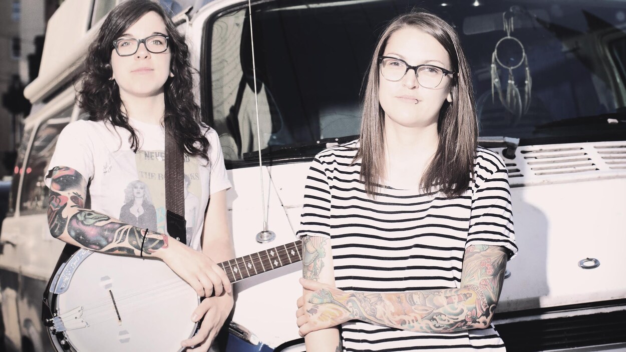 The Johans, un duo folk de la relève. On aperçoit deux filles, dont l'une avec un banjo, devant une camionnette. The Johans, un duo folk de la relève. On aperçoit deux filles, dont l'une avec un banjo, devant une camionnette.