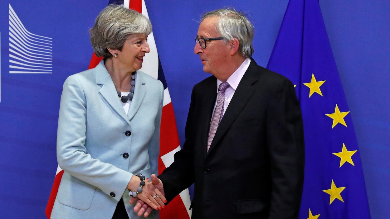 Theresa May serre la main de Jean Claude Juncker sur fond de drapeaux britannique et européen