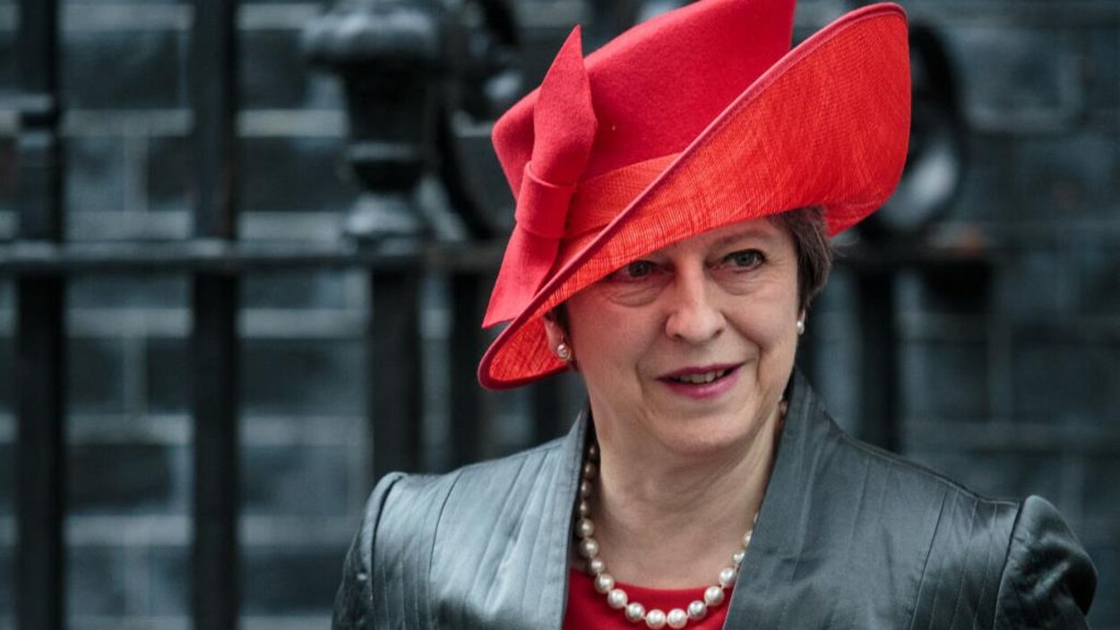 Plan rapproché de Mme May, qui porte un grand chapeau asymétrique. Plan rapproché de Mme May, qui porte un grand chapeau asymétrique.