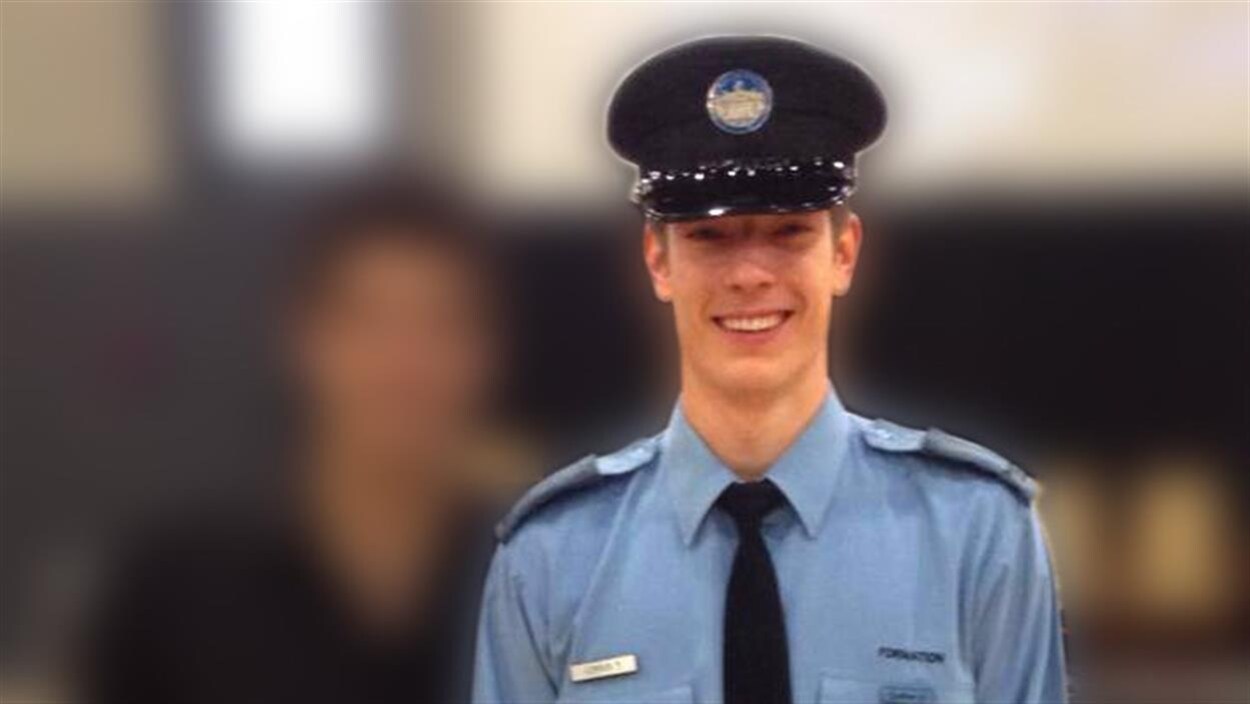 Un jeune policier en uniforme est souriant alors qu'il se fait photographier.