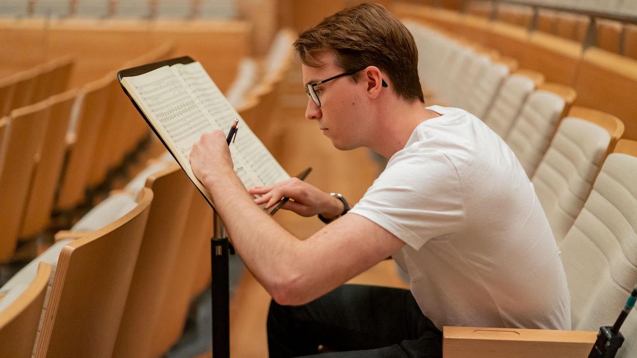 Thomas Le Duc-Moreau, assis dans la Maison symphonique de Montréal, écrit sur une partition posée sur un lutrin.