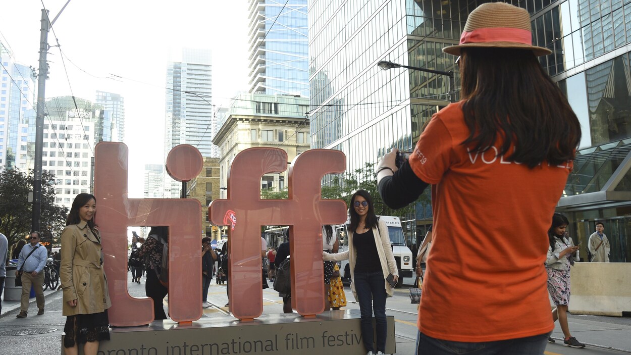 Une bénévole prend une photo de deux jeunes femmes devant un logo géant du TIFF.