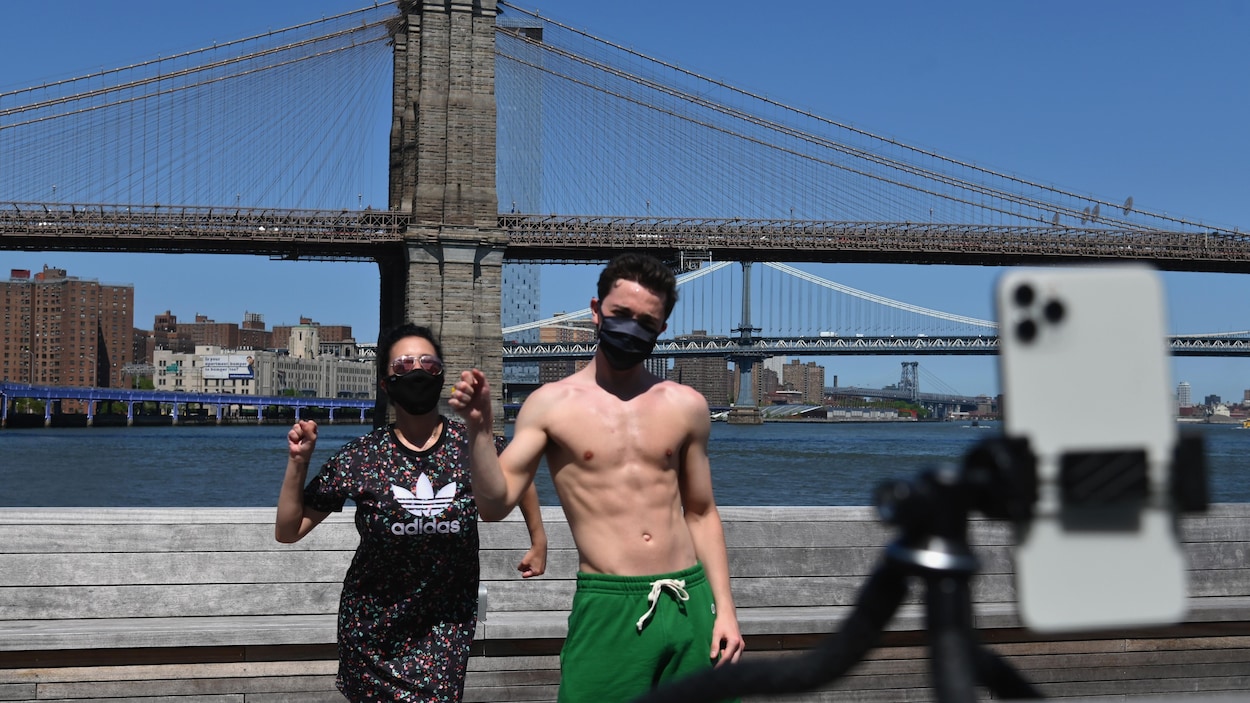 Une femme et un homme dansent devant le pont de Brooklyn. La scène est captée par un téléphone cellulaire sur un trépied.