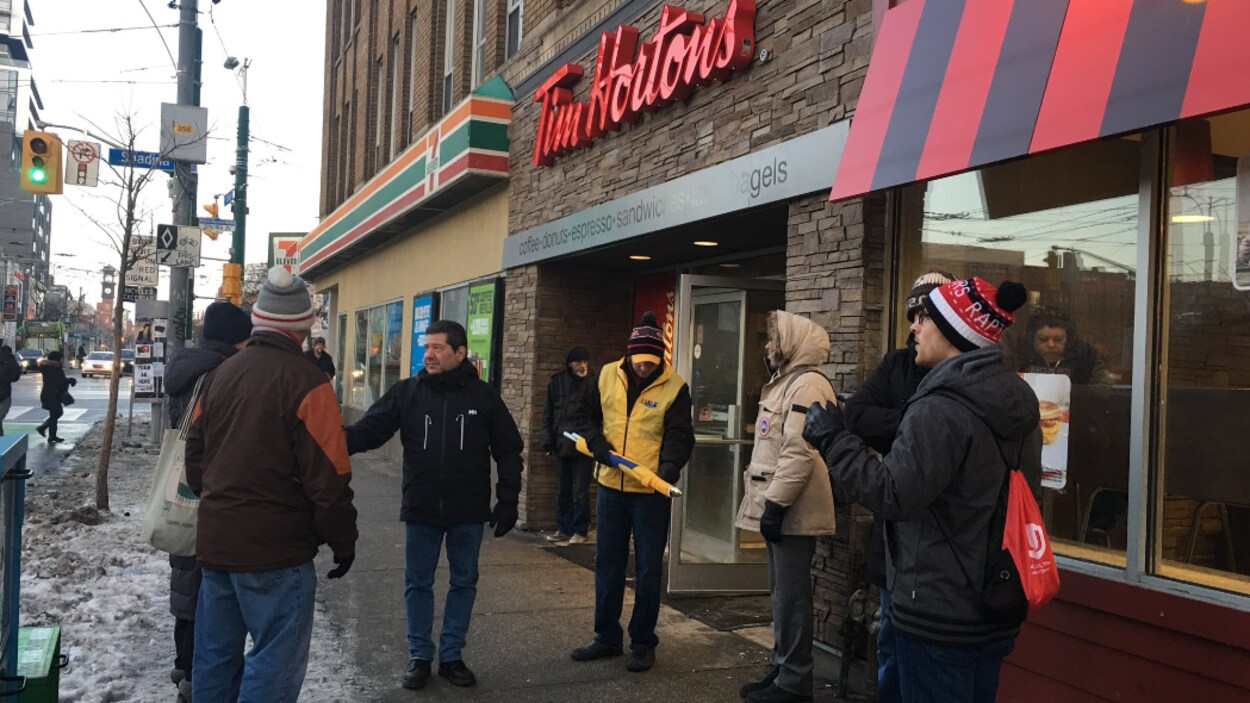 Photo de personnes vêtues de manteaux se tenant à l'entrée d'un Tim Hortons. Photo de personnes vêtues de manteaux se tenant à l'entrée d'un Tim Hortons.