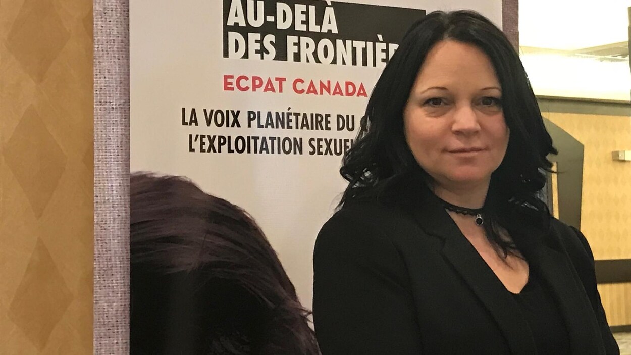 Une femme devant une grande affiche sur laquelle est écrit : Au delà des frontières. Une femme devant une grande affiche sur laquelle est écrit : Au delà des frontières.