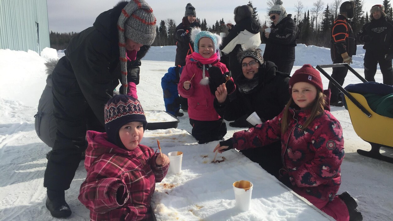 Des enfants et des parents qui dégustent de la tire sur la neige.