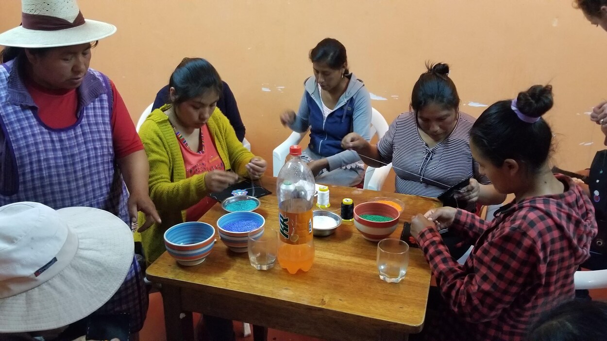 Des tisserandes quechuas sont assises autour d'une table et fabriquent des ceintures fléchées.