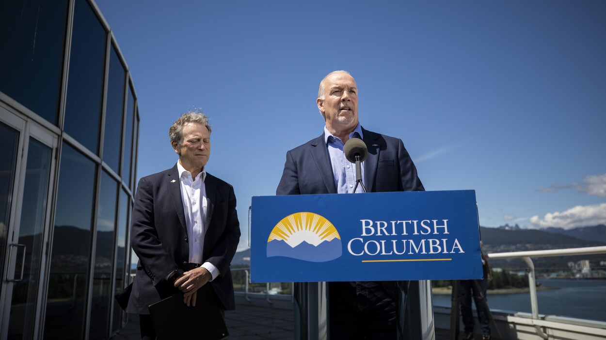 John Horgan derrière un lutrin accompagné de son ministre de l'environnement.