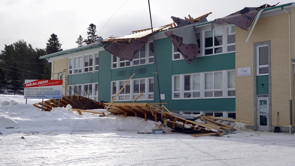 Plusieurs poutres et planches de bois jonchent le sol devant une école de deux étages.
