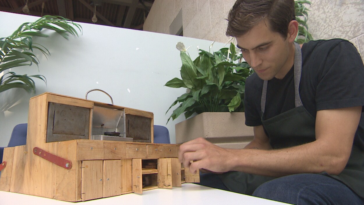 Tom Brown assis avec sa mini-cuisine en bois.
