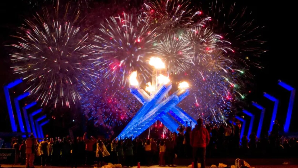 Des gens regardent les feux d'artifice et la flamme olympique.