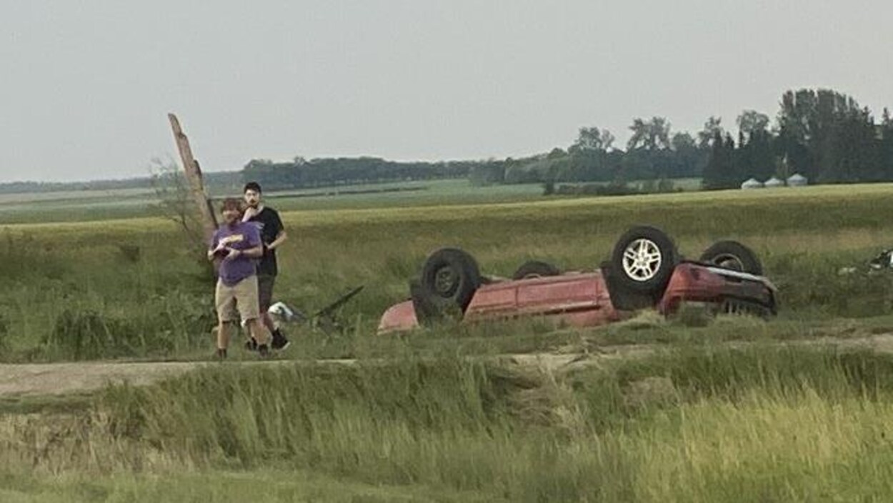 Deux personnes près d'une voiture renversée dans un champ.