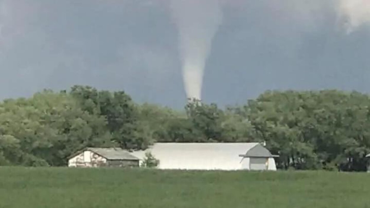 Paysage de campagne au-dessus duquel s'élève un cône de tornade
