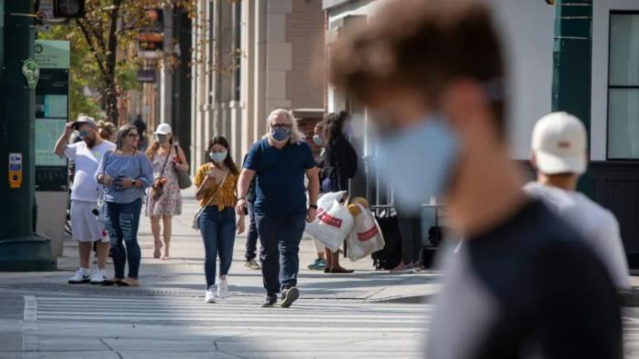 Des gens marchent dans la rue avec un masque.