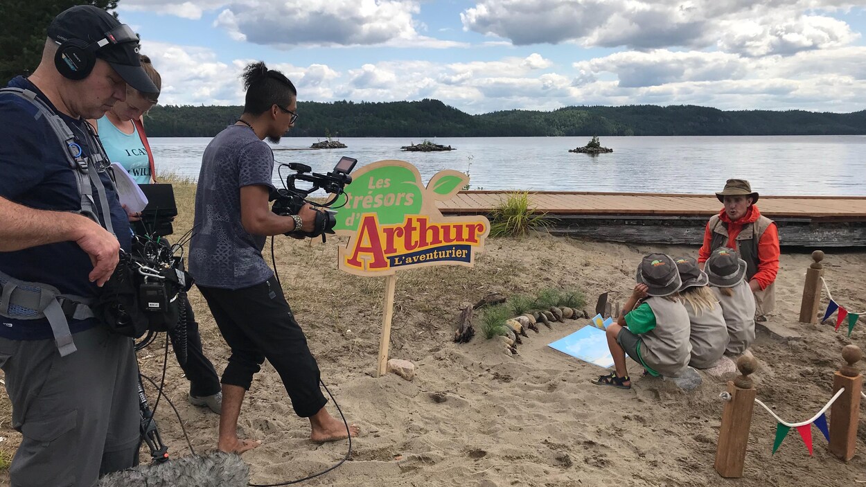 Une équipe de tournage filme Arthur L'aventurier et des enfants sur une plage.