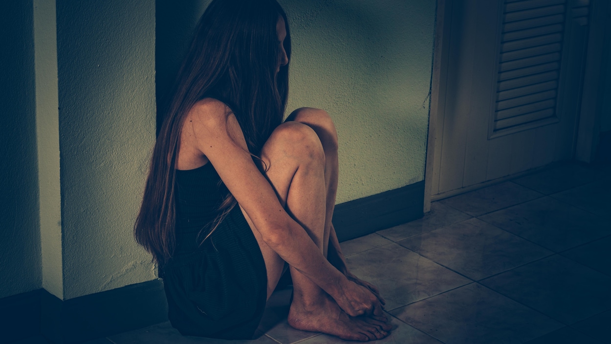 Une femme recroquevillée sur le sol dans une pièce.