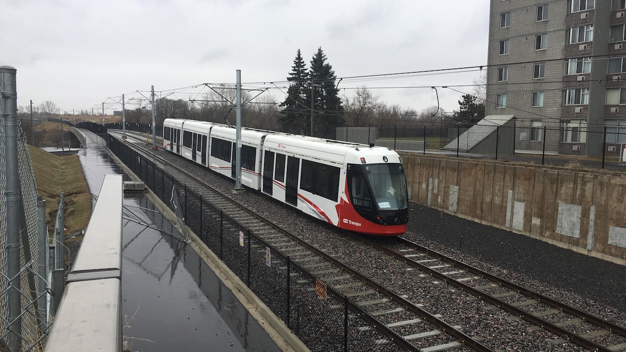Le train comprend quatre wagons et circule derrière un édifice.