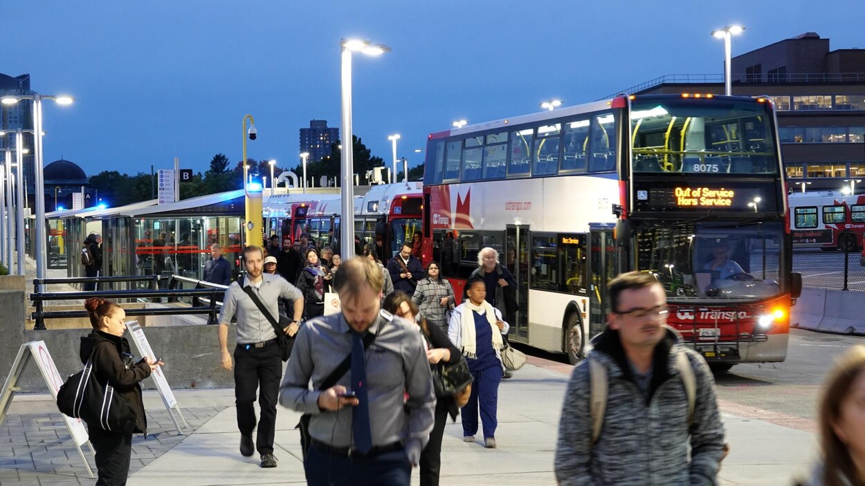 Des gens quittent l'autobus pour se rendre à une gare du train léger