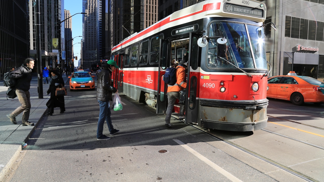 Des Torontois embarquent dans un tramway à un arrêt.