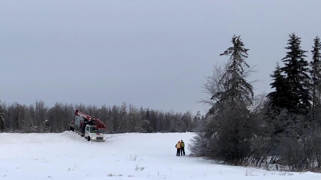 Deux hommes sur le bord de la route regardent un camion immobilisé dans la neige sur un talus.