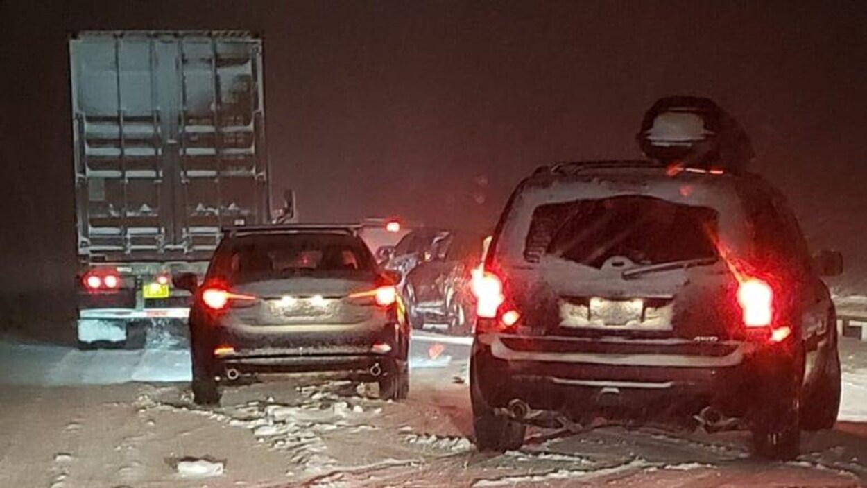 Des voitures et un camion sont immobilisés sur une autoroute glacée et enneigée.