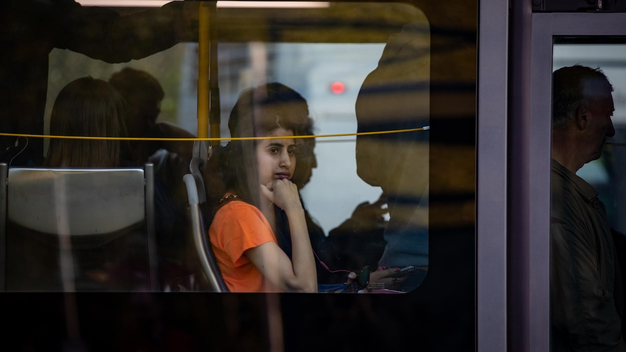Une femme assise dans un autobus bondé regarde par la fenêtre.