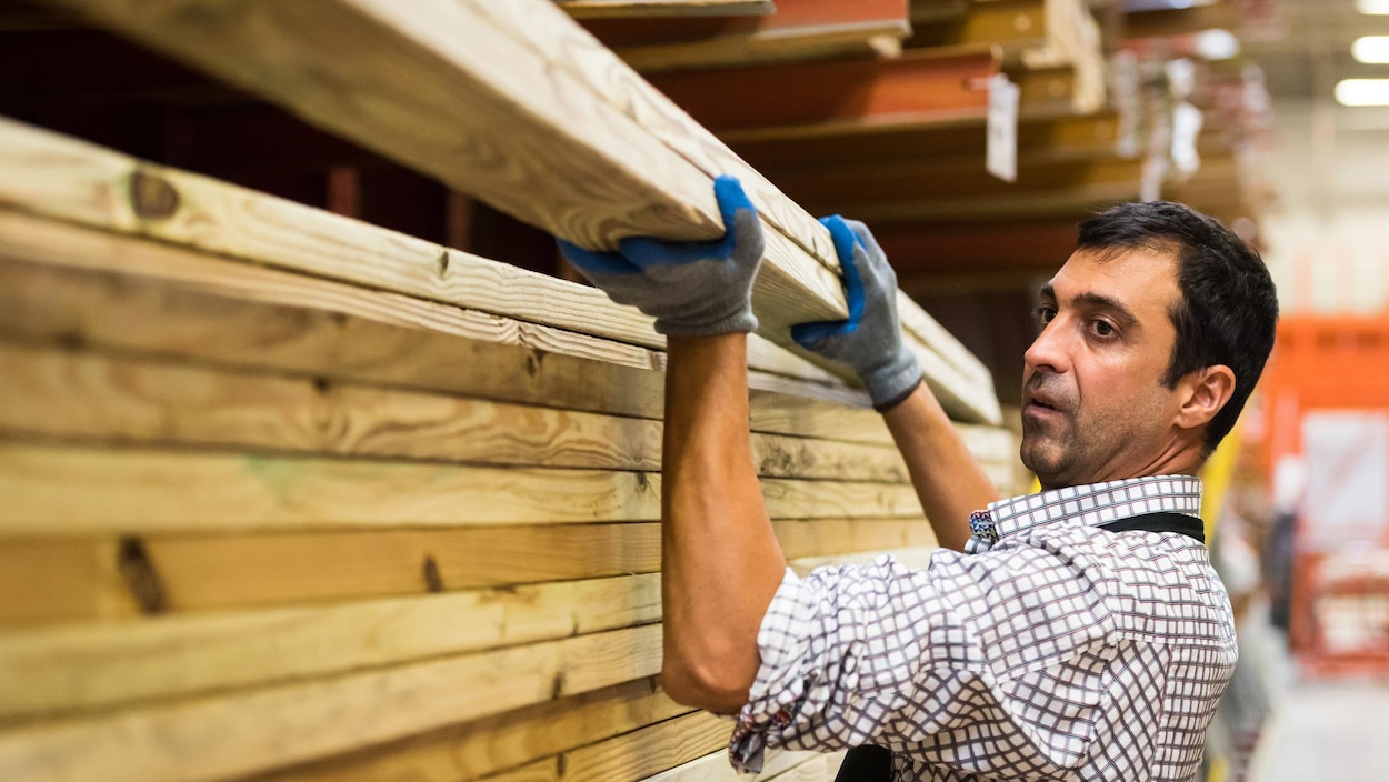 Un travailleur soulève des planches de bois.