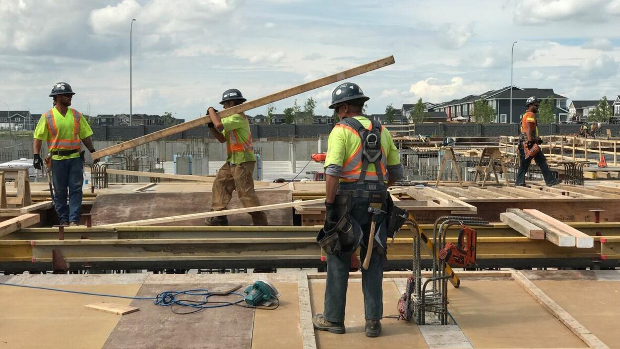 Des travailleurs de la construction déambulent sur un toit, un d'entre eux transportant une longue planche.