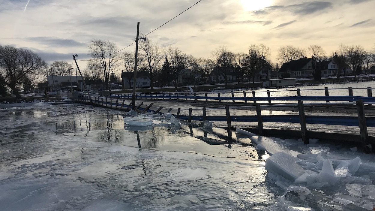 On voit un ponton sur l'eau dont les barrières sont toutes déformées pas de gros morceaux de glace.