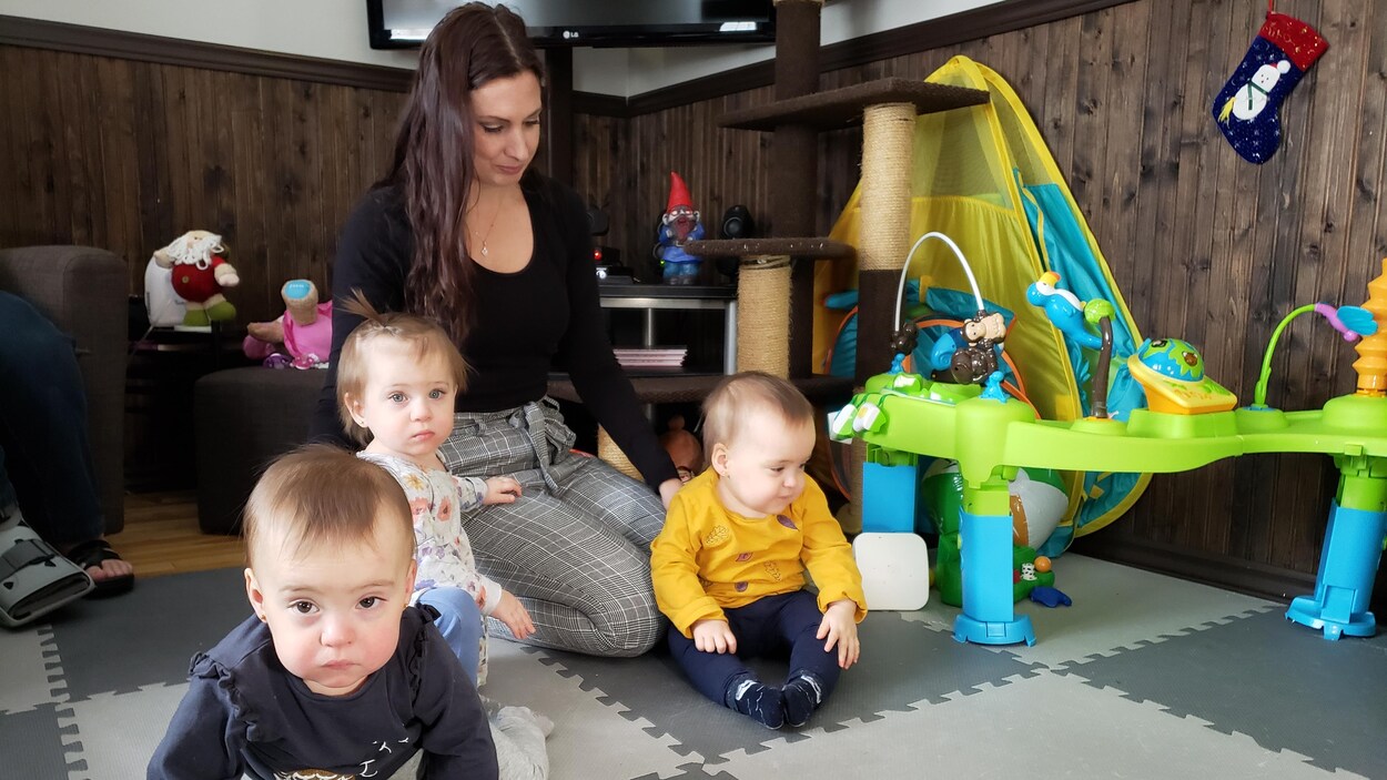 Trois enfants sur un tapis de jeu avec leur mère à l'arrière