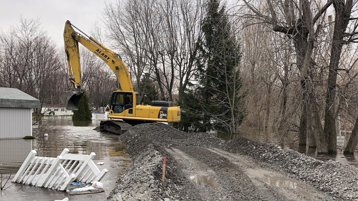 Une pelle excavatrice dépose du gravier dans l'eau.