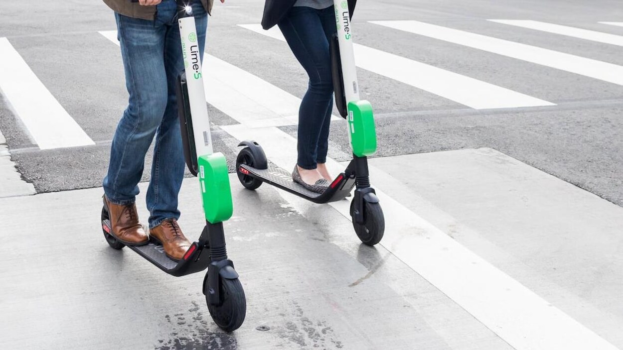 Deux personnes circulent en trottinette dans un environnement urbain.