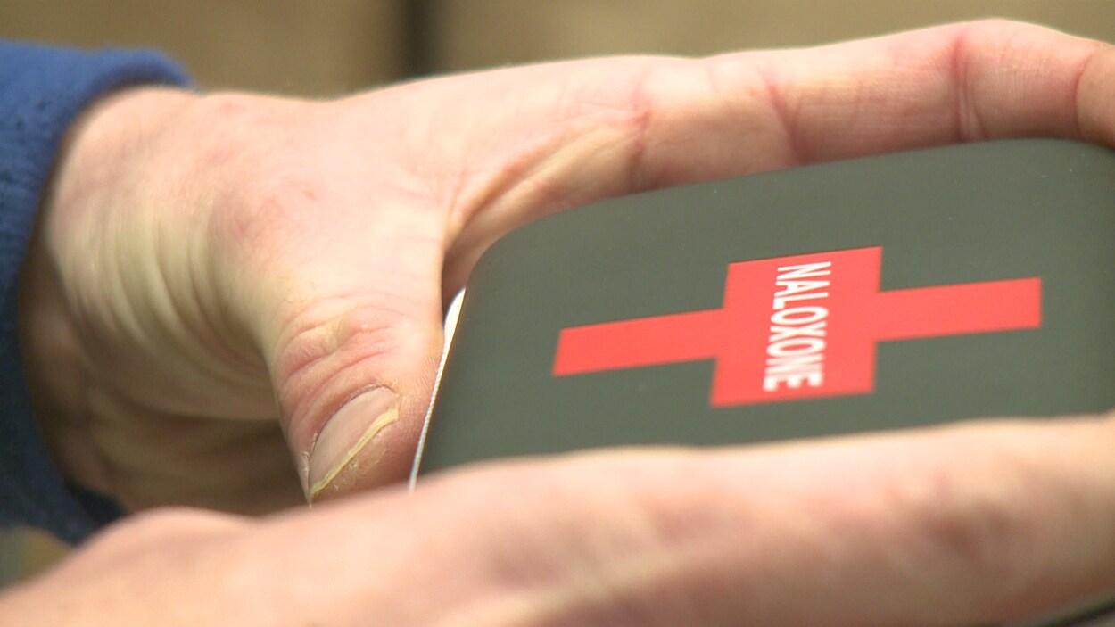 Gros plan sur des mains qui tiennent une petite boîte carrée avec une croix rouge sur laquelle est inscrit naloxone. Gros plan sur des mains qui tiennent une petite boîte carrée avec une croix rouge sur laquelle est inscrit naloxone.