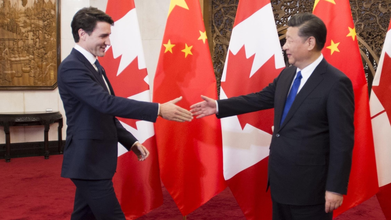 Justin Trudeau et le président chinois Xi Jinping, devant des drapeaux de la Chine et du Canada, sur le point de se serrer la main.