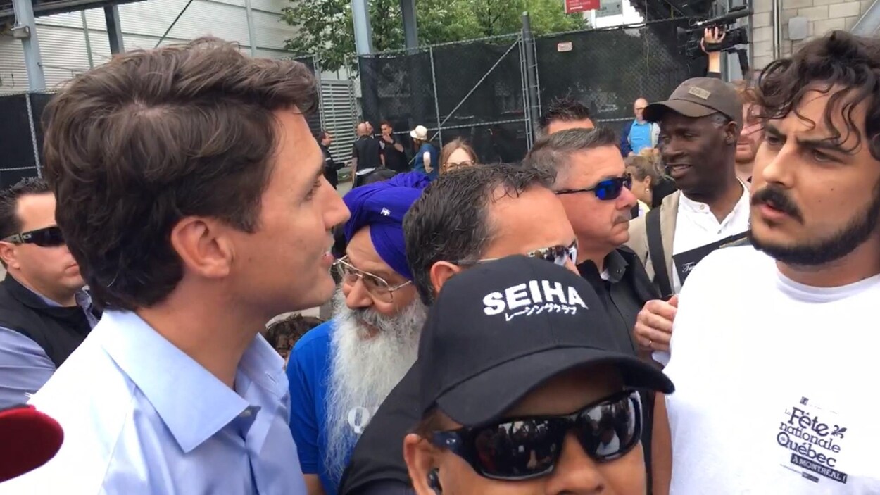 Le premier ministre Justin Trudeau regarde un jeune homme portant une barbe et visiblement mécontent de sa présence. Ils sont entourés d'une foule de personnes. Le premier ministre Justin Trudeau regarde un jeune homme portant une barbe et visiblement mécontent de sa présence. Ils sont entourés d'une foule de personnes.