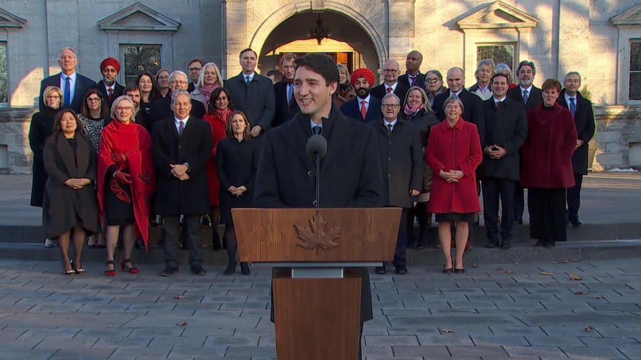 Justin Trudeau au micro, à l'extérieur du parlement, alors que ses ministres sont rassemblés derrière lui.