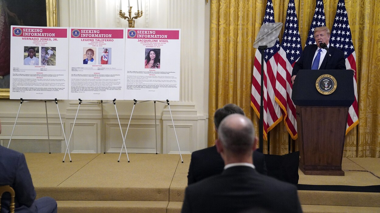 Donald Trump parlant devant un auditoire, avec un drapeau américain derrière lui et des photographies d'enfants qui ont été victimes de crimes.