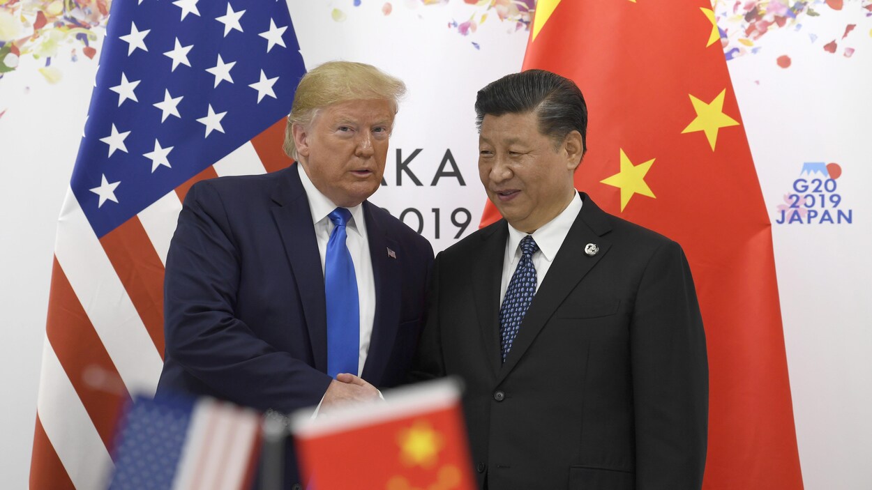 Donald Trump serre la main de Xi Jinping devant leur drapeau respectif.