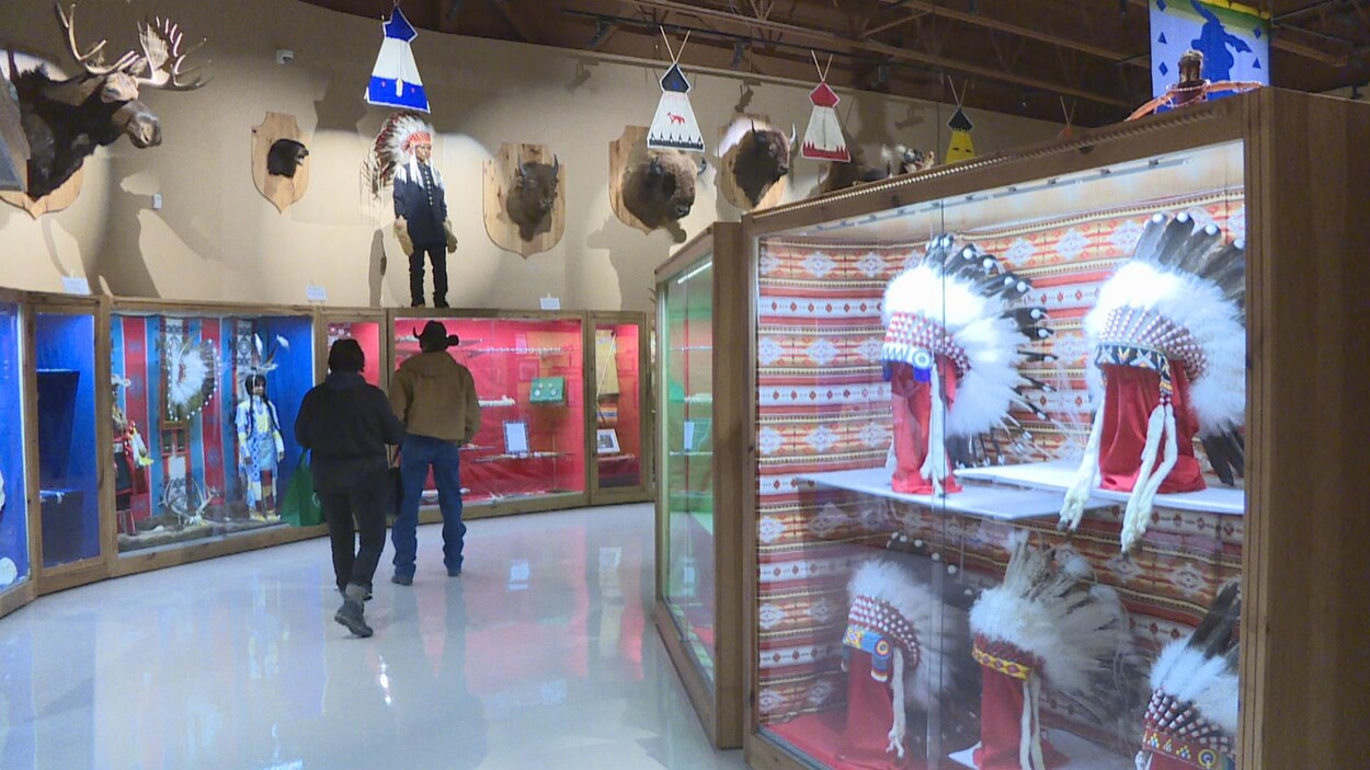 Deux hommes de dos explorent le musée. À droite, il y a des coiffures traditionnelles autochtones derrière des vitrines, à gauche, des vêtements traditionnels.
