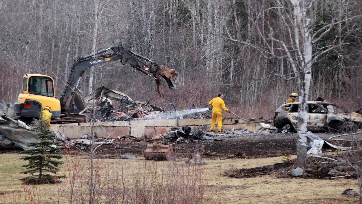Des hommes habillés en jaune arrosent avec des boyaux une voiture incendiée.