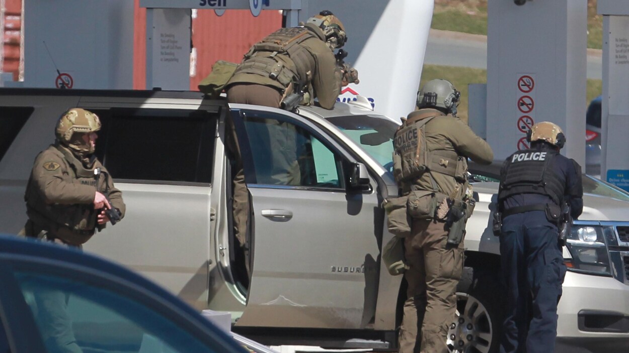 Quatre policiers derrière un véhicule, pointant leurs armes.