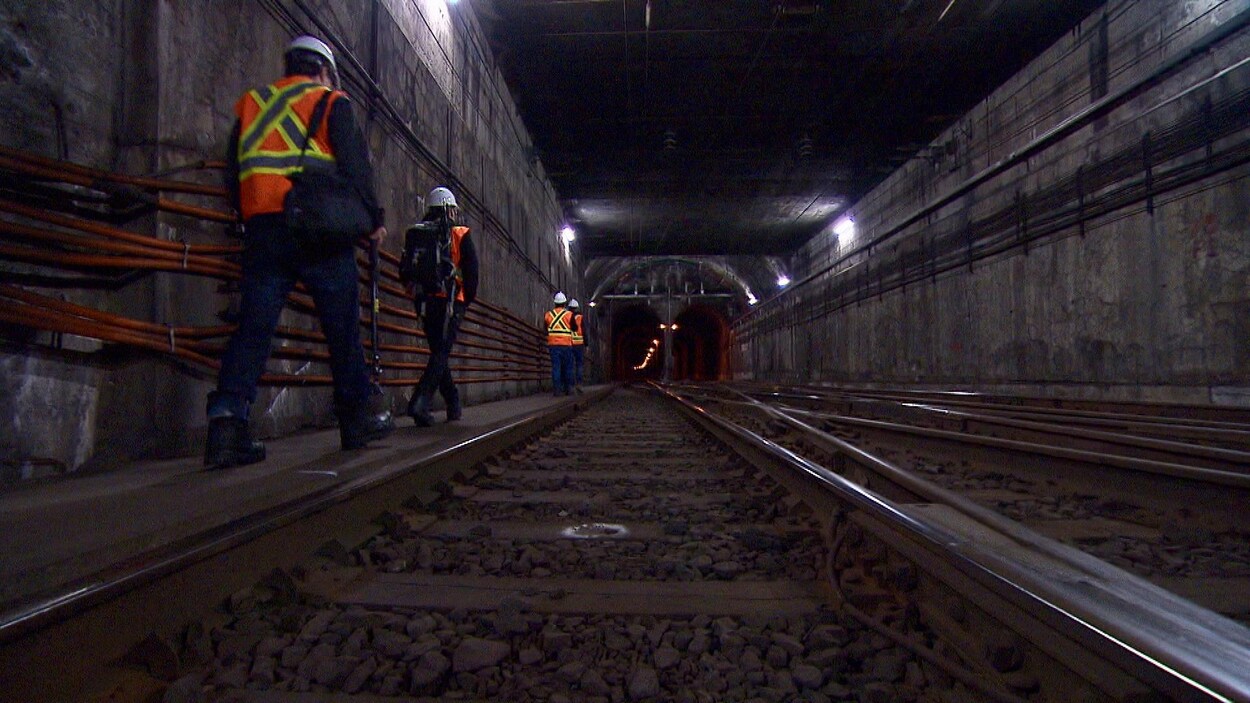 Des hommes vêtus de vestes réfléchissantes s'engouffrent dans le tunnel.