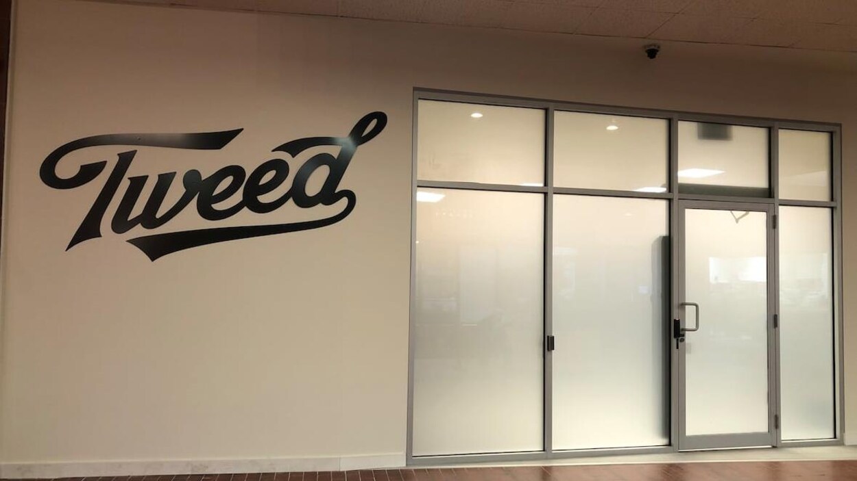 Sur un mur blanc, il est écrit Tweed en grand et en noir à côté d'une porte et de fenêtres en verre givré.