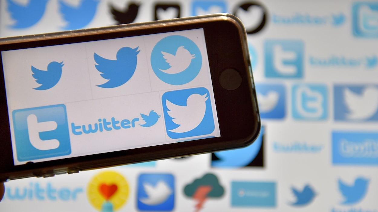 Des logos de Twitter sont visibles sur un téléphone cellulaire et sur un écran en arrière-plan.
