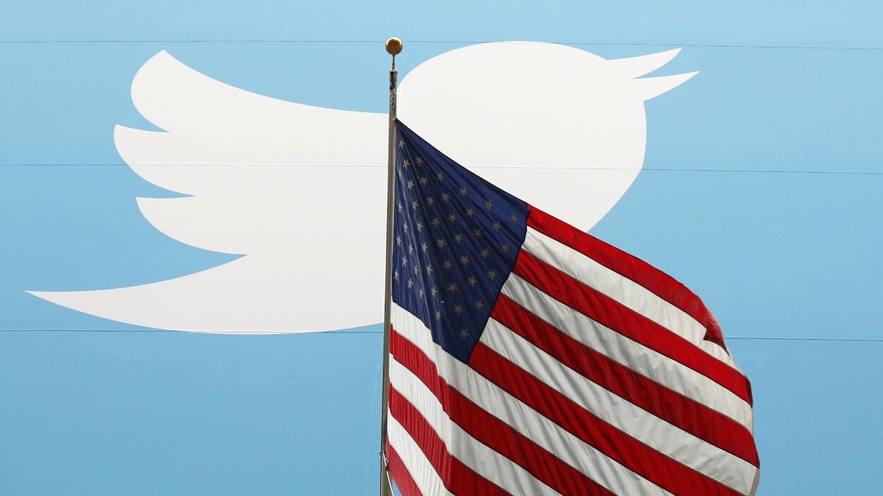 Le logo du réseau social twitter est placé derrière un drapeau des États-Unis.